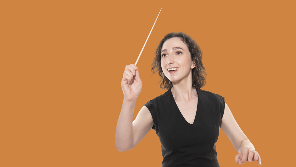 A female student, wearing a black top, waving her conductor's baton, against a warm orange background.